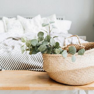 Eucalyptus in a basket with a bed covered in black and white cotton sheets 