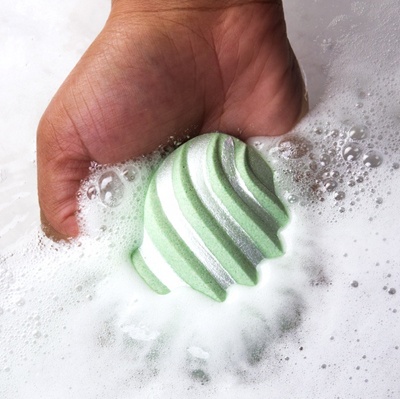 A bath bomb in a hand partially sumberged in water, foaming