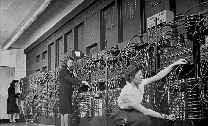 a black and white photo of a team of women operating a large computer