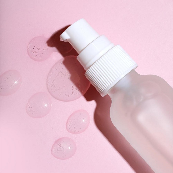a bottle of clear face serum on a pink background