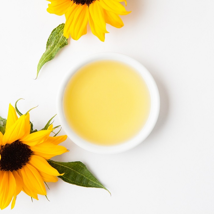 A bowl of sunflower oil with two
                sunflowers on a white background.